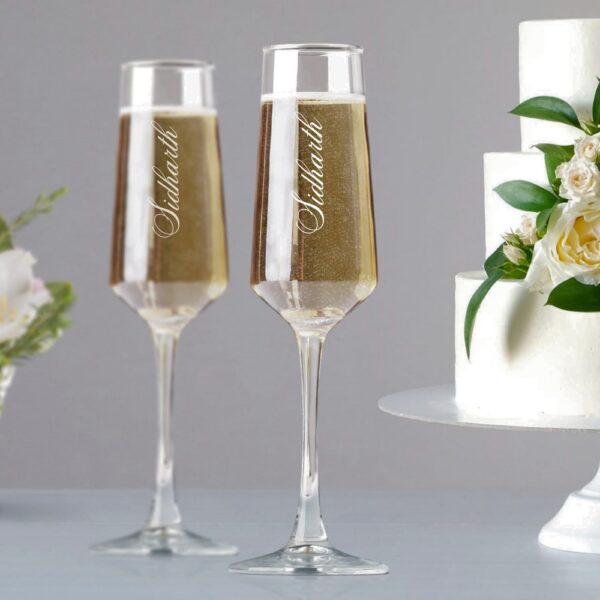 Elevate your special celebrations with these exquisite personalized champagne flutes. Each glass features a contemporary geometric design with an elegant, elongated stem that adds sophistication to any occasion. The crystal-clear glassware is enhanced with deep, precision-engraved customisation that maintains its beauty through countless toasts. These premium flutes come as a matching set of two, perfect for wedding ceremonies, anniversaries, or any momentous occasion. The modern angular bowl design helps preserve the bubbles while concentrating the champagne's aroma. The sturdy base ensures stability, whilst the tall, graceful stem allows for proper holding without warming the champagne. These bespoke glasses make for a treasured keepsake that couples can use to celebrate their special moments for years to come. Each flute is carefully crafted to hold the perfect amount of champagne, making them ideal for those celebratory toasts. The sophisticated design complements any table setting, from casual gatherings to formal events.
