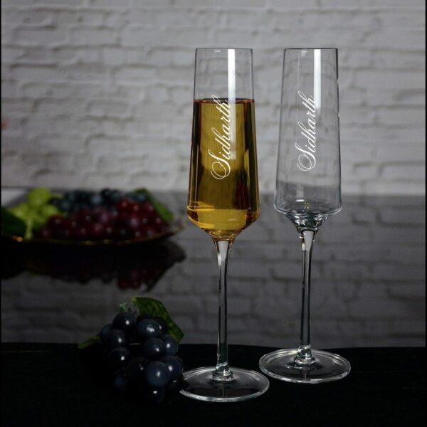 Elevate your special celebrations with these exquisite personalized champagne flutes. Each glass features a contemporary geometric design with an elegant, elongated stem that adds sophistication to any occasion. The crystal-clear glassware is enhanced with deep, precision-engraved customisation that maintains its beauty through countless toasts. These premium flutes come as a matching set of two, perfect for wedding ceremonies, anniversaries, or any momentous occasion. The modern angular bowl design helps preserve the bubbles while concentrating the champagne's aroma. The sturdy base ensures stability, whilst the tall, graceful stem allows for proper holding without warming the champagne. These bespoke glasses make for a treasured keepsake that couples can use to celebrate their special moments for years to come. Each flute is carefully crafted to hold the perfect amount of champagne, making them ideal for those celebratory toasts. The sophisticated design complements any table setting, from casual gatherings to formal events.