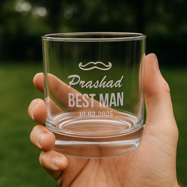 Personalized whiskey glass engraved with a mustache design, the name 'Prashad', text 'BEST MAN', and the date 10.02.2025, displayed on a wooden surface with a warm background