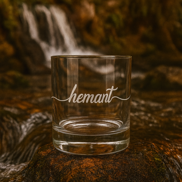 Personalized crystal whiskey glass with deep engraving of the name Hemant, filled with whiskey and ice cubes