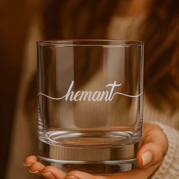 Personalized crystal whiskey glass with deep engraving of the name Hemant, filled with whiskey and ice cubes