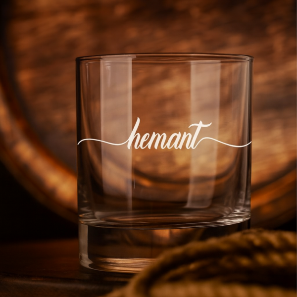 Personalized crystal whiskey glass with deep engraving of the name Hemant, filled with whiskey and ice cubes
