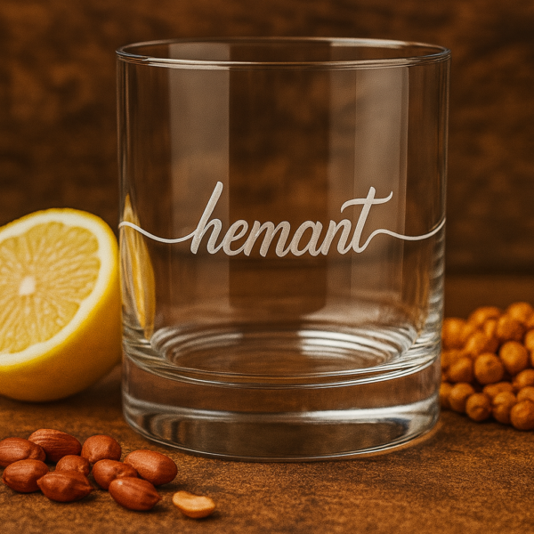 Personalized crystal whiskey glass with deep engraving of the name Hemant, filled with whiskey and ice cubes