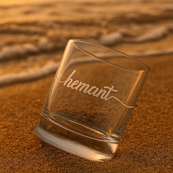 Personalized crystal whiskey glass with deep engraving of the name Hemant, filled with whiskey and ice cubes
