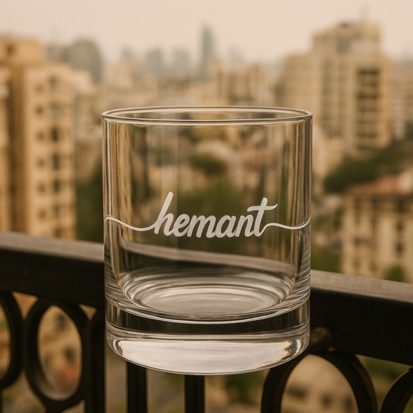 Personalized crystal whiskey glass with deep engraving of the name Hemant, filled with whiskey and ice cubes