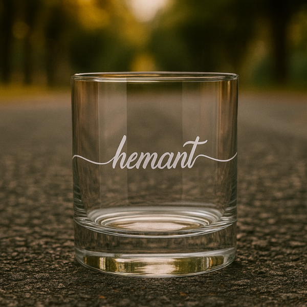 Personalized crystal whiskey glass with deep engraving of the name Hemant, filled with whiskey and ice cubes