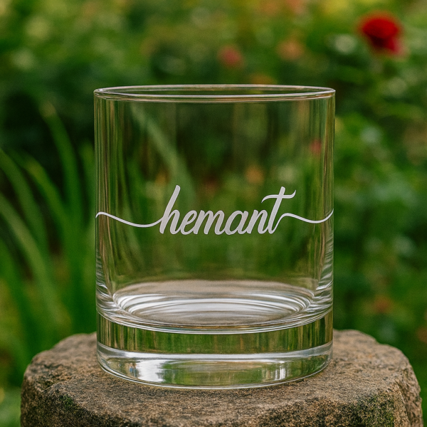 Personalized crystal whiskey glass with deep engraving of the name Hemant, filled with whiskey and ice cubes
