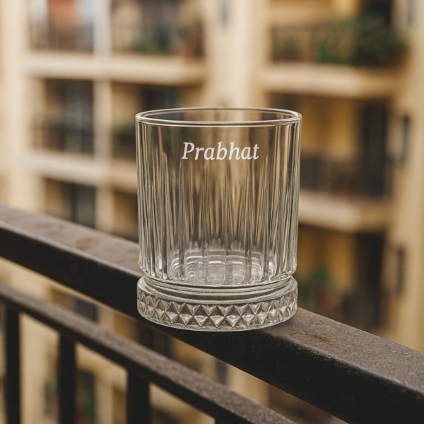 Personalized engraved whiskey glass with name 'Prabhat' on the side and bottom message 'I Promise to Always Be by Your Side', displayed outdoors on grass
