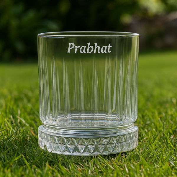 Personalized engraved whiskey glass with name 'Prabhat' on the side and bottom message 'I Promise to Always Be by Your Side', displayed outdoors on grass